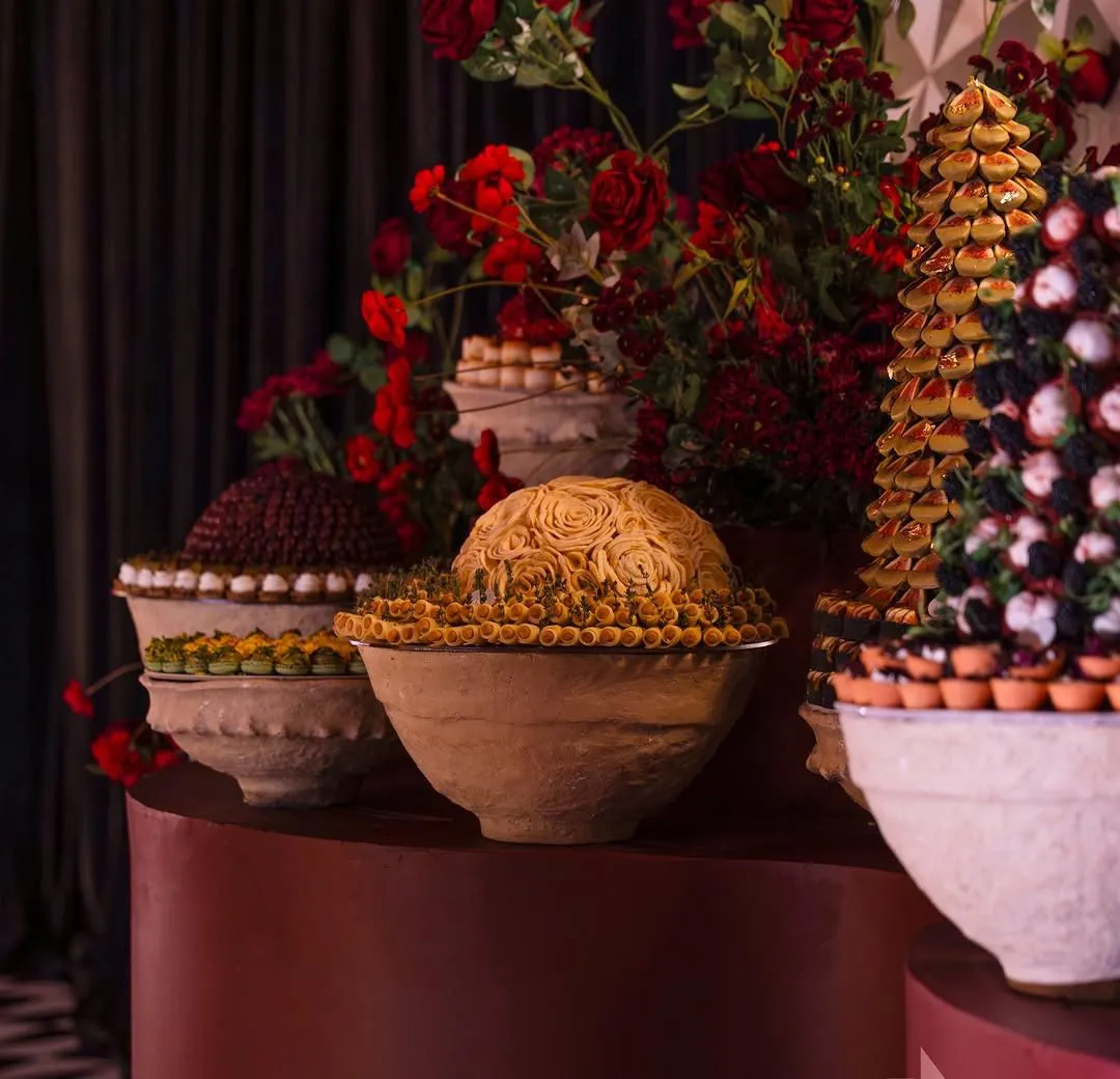 Stone bowls of pastries beside a chocolate tower and red roses