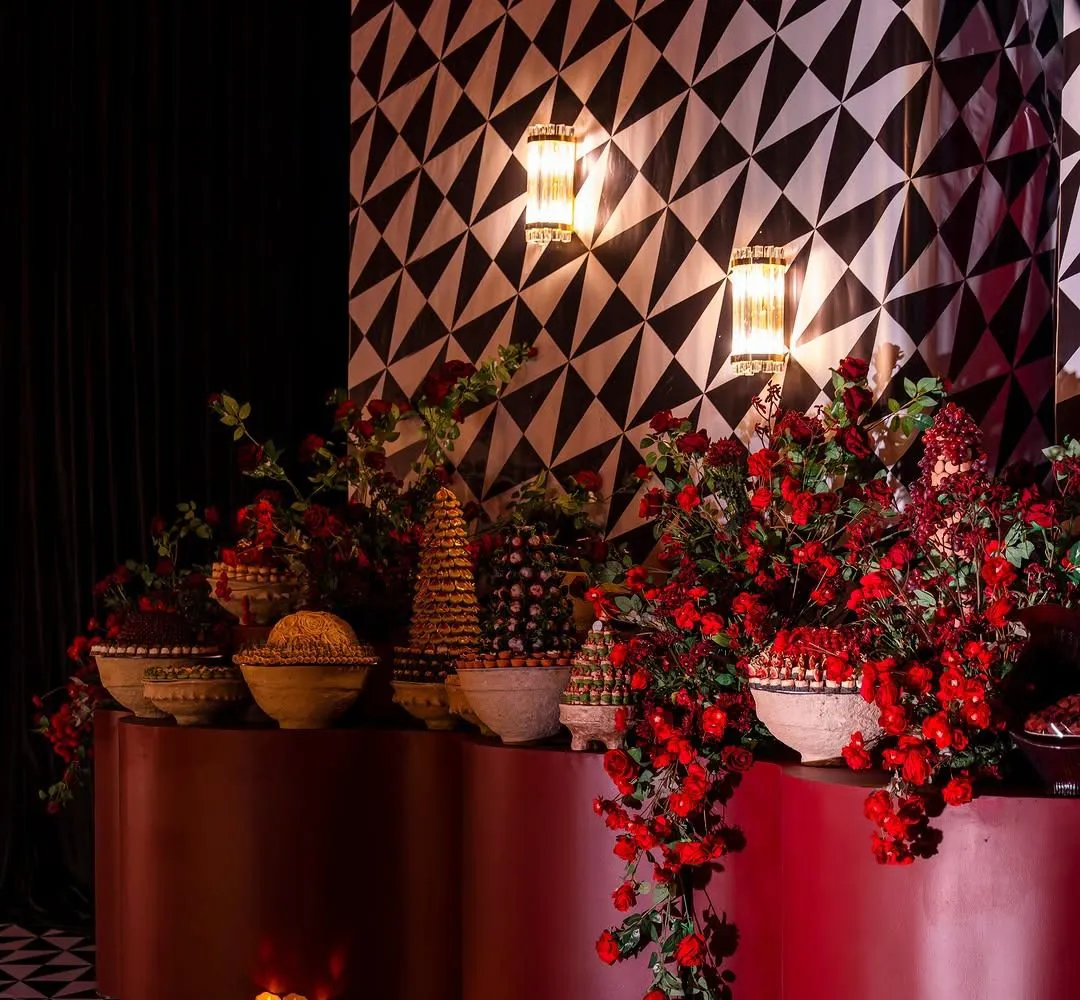 Dessert table on burgundy pedestals with red roses against a geometric wall