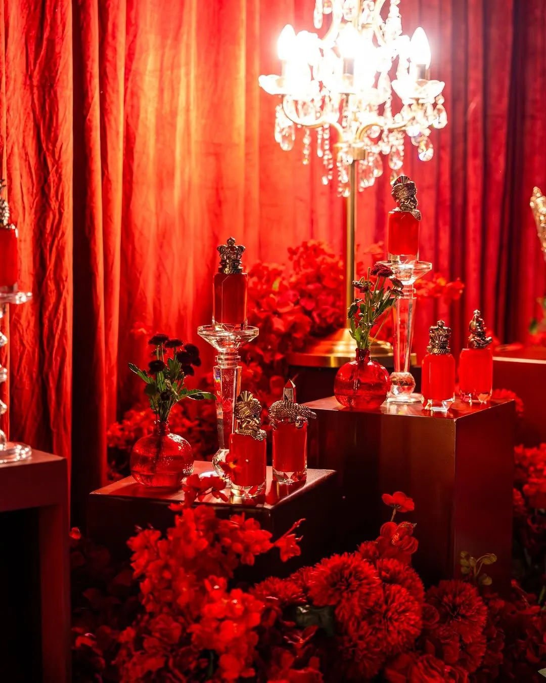 Perfume display with red bottles before red curtains and a crystal chandelier